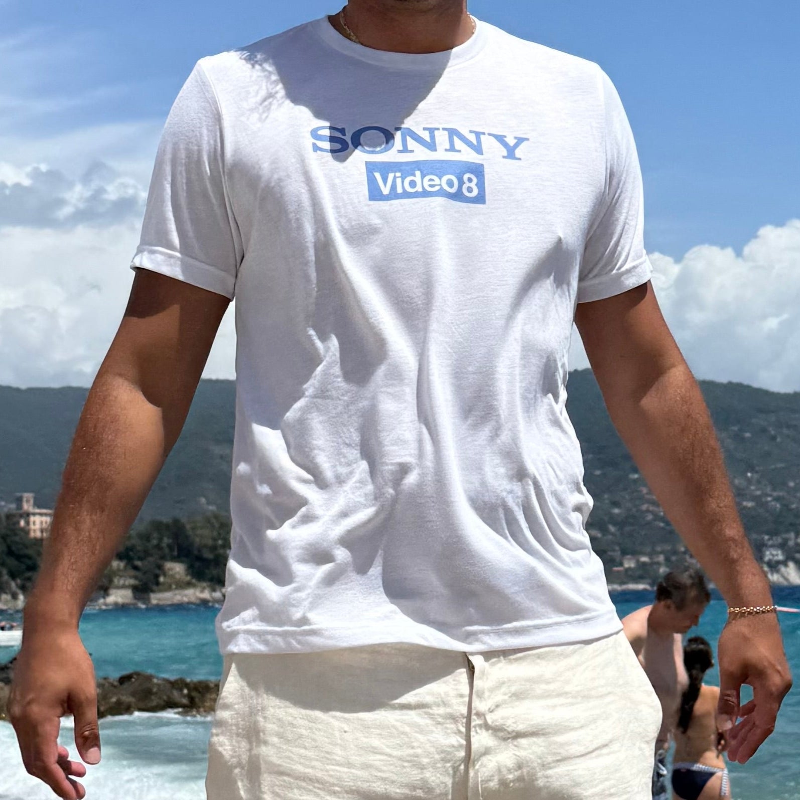 Person wearing a white t-shirt with 'SONNY Video' text on a beach